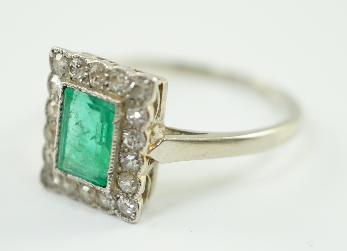 A 1920's 18ct white gold and platinum, emerald and millegrain set diamond rectangular cluster ring